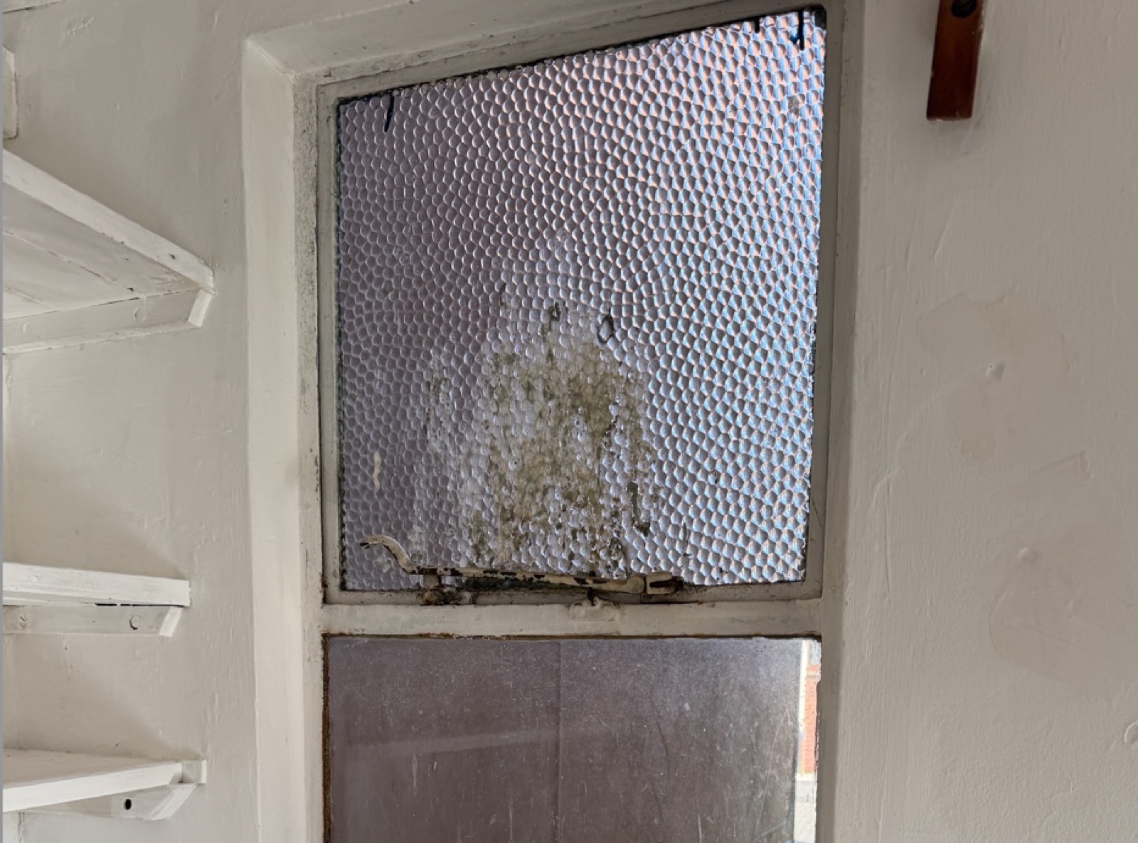 Original Crittall steel-framed window with reeded textured glass, showing significant rust at the bottom of the frame, condensation damage, and a corroded handle — typical of unrestored Crittall windows in pre-war Hertfordshire properties